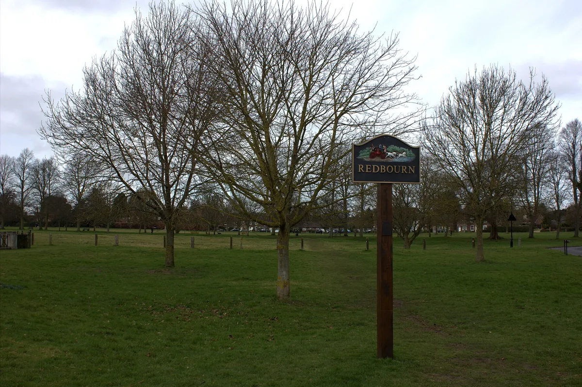 The Redbourn village sign on a post on Redbourn Common, with bare trees and open grass behind