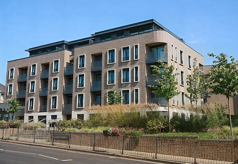 A four and five storey brick block of flats with balconies and a curved corner, behind ornamental grasses and a low railing on Victoria Street
