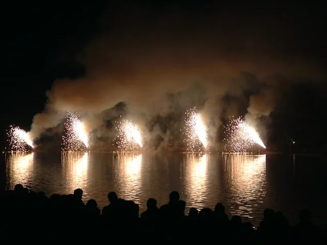 Fireworks fountains set off across the lake in Verulamium Park at night, with the crowd in silhouette on the near bank